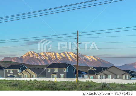 Neighborhood homes with sunlit snow capped mountain and blue sky background Neighborhood homes with sunlit snow capped mountain and blue sky background 71771433