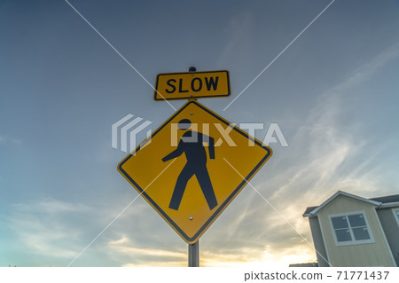 Yellow Slow sign and pedestrian crossing sign against cloudy sky at sunset Yellow Slow sign and pedestrian crossing sign against cloudy sky at sunset 71771437