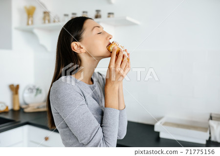 Portrait of rejoicing woman eats tasty croissant at home. 71775156