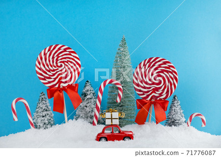 Red Santa car with gift on roof in Christmas tree forest with candies and lollipops sweets. Merry Christmas and Happy New Year Red Santa car with gift on roof in Christmas tree forest with candies and lollipops sweets. Merry Christmas and Happy New Year 71776087