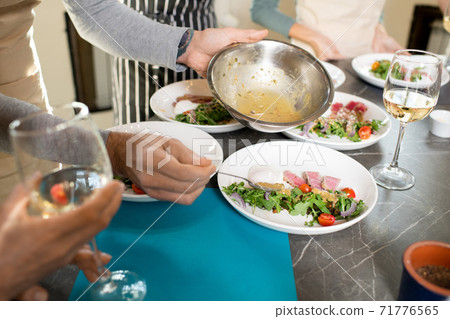 Hands of mature man putting sauce from metallic bowl on plate with salad 71776565