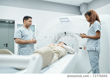 Young nurse or assistant in uniform making notes while standing by couchette 71776848