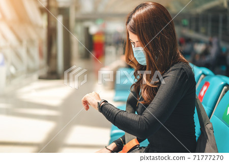 Asian woman wearing medical protective face mask looking at her wrist watch for checking time in terminal lounge at airport, Healthcare and infection concept. Asian woman wearing medical protective face mask looking at her wrist watch for checking time in terminal lounge at airport, Healthcare and infection concept. 71777270