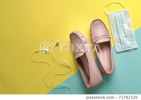 Stylish women shoes, ear phones and medical face mask on yellow and blue background. 71782326