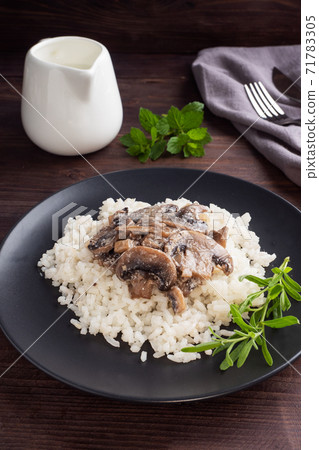 Risotto with mushrooms on a black plate. Boiled white rice with champignons in cream sauce. Dark wooden background. 71783305