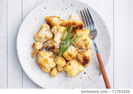 Fried cauliflower florets in batter on a white plate. White wooden background. Fried cauliflower florets in batter on a white plate. White wooden background. 71783306