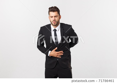 Unhappy man with stomach pain spasm. portrait of handsome bearded businessman in suit. Indoor studio shot, isolated on grey background 71786461