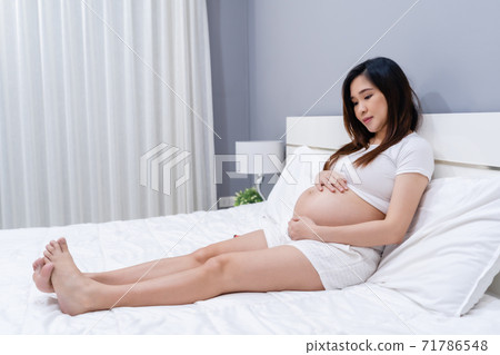 pregnant woman stroking her belly on bed 71786548