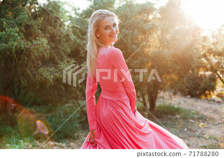 Beautiful blonde woman in pink dress walks in the park at sunset 71788280