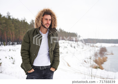 Attractive bearded man standing outdoors in winter season forest. Attractive bearded man standing outdoors in winter season forest. 71788839