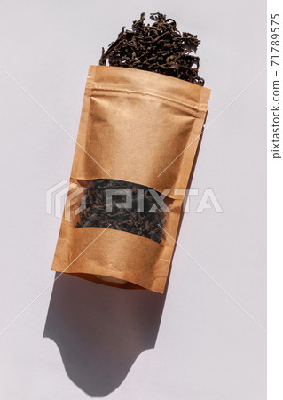 Brown kraft paper pouch bags with tea leaves top view with harsh shadow on white background. Coffee packaging flat lay. Brown kraft paper pouch bags with tea leaves top view with harsh shadow on white background. Coffee packaging flat lay. 71789575