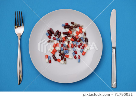 Lots of multi-colored capsule and lying on plate with fork and knife closeup Lots of multi-colored capsule and lying on plate with fork and knife closeup 71790031