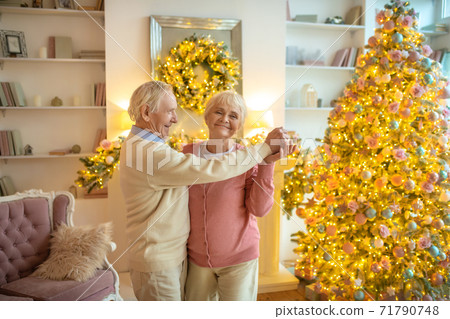 Senior couple dancing near christmas tree and looking happy 71790748