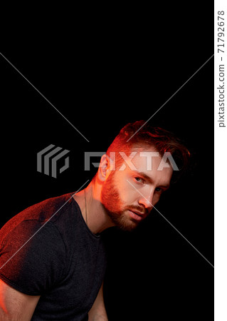 A brutal man on a dark background in the light of a red lamp. 71792678