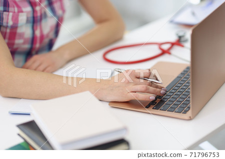 Female hands are working on laptop next to stethoscope. 71796753