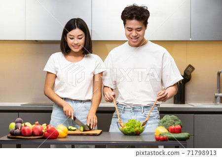 Cheerful Korean Couple Making Fresh Veggie Salad Standing In Kitchen Cheerful Korean Couple Making Fresh Veggie Salad Standing In Kitchen 71798913