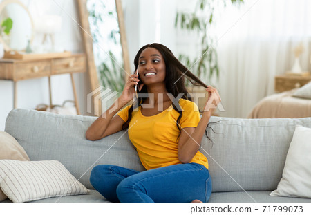 Portrait of gorgeous black woman speaking on mobile phone and smiling while relaxing on sofa at home Portrait of gorgeous black woman speaking on mobile phone and smiling while relaxing on sofa at home 71799073