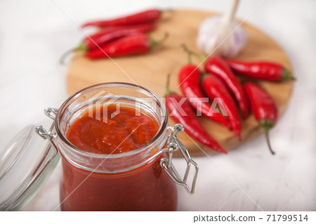 Harissa in a glass jar close-up and hot chili peppers on a white background. Harissa in a glass jar close-up and hot chili peppers on a white background. 71799514