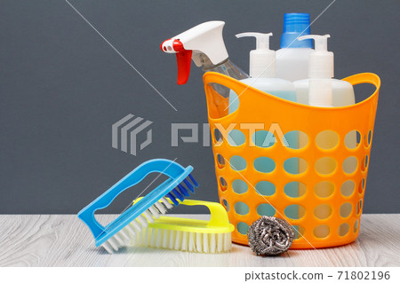 Bottles of dishwashing liquid, brushes and sponge in a basket on wooden desk. Bottles of dishwashing liquid, brushes and sponge in a basket on wooden desk. 71802196