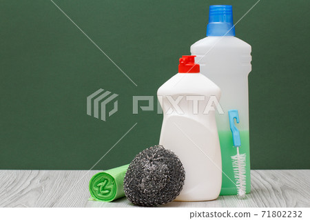 Bottles of dishwashing liquid, brush, garbage bags and sponge on green background. 71802232