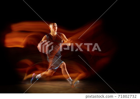 Young east asian basketball player in action and jump in mixed light over dark studio background. Concept of sport, movement, energy and dynamic, healthy lifestyle. 71802732