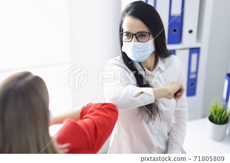 Two women in medical protective masks greet each other in office. Two women in medical protective masks greet each other in office. 71805809