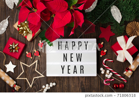 Happy New Year text on white Lightbox with red flower poinsettia, Christmas decorations, gift boxes on dark wooden background. Happy New Year text on white Lightbox with red flower poinsettia, Christmas decorations, gift boxes on dark wooden background. 71806318