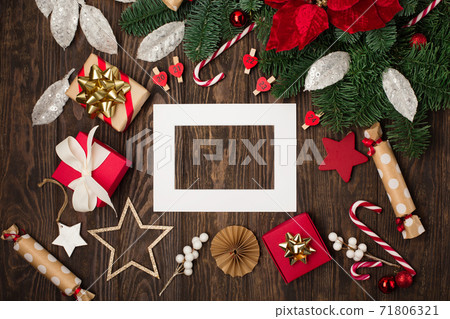 Empty white holiday frame, red flower poinsettia, Christmas decorations, gift boxes, candy canes on dark wooden background. Empty white holiday frame, red flower poinsettia, Christmas decorations, gift boxes, candy canes on dark wooden background. 71806321