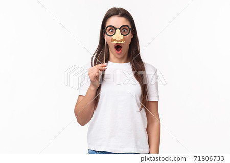 Entertainment, fun and holidays concept. Funny and cute young girl fool around, praying wearing glasses and nose mask, gasping amazed, look surprised standing white background Entertainment, fun and holidays concept. Funny and cute young girl fool around, praying wearing glasses and nose mask, gasping amazed, look surprised standing white background 71806733