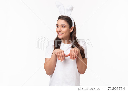 Portrait of funny and cute, playful adult girl in t-shirt and rabbit ears, look away with amused happy face, imitating bunny with paws and silly grin, look away, standing white background Portrait of funny and cute, playful adult girl in t-shirt and rabbit ears, look away with amused happy face, imitating bunny with paws and silly grin, look away, standing white background 71806734
