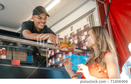 Cook in a food truck handing tasty burger over to woman customer Cook in a food truck handing tasty burger over to woman customer 71806906