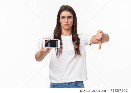 Communication, technology and lifestyle concept. Portrait of upset and disappointed young female rated bad app, showing content on mobile phone, grimacing dislike, show thumbs-down disapproval Communication, technology and lifestyle concept. Portrait of upset and disappointed young female rated bad app, showing content on mobile phone, grimacing dislike, show thumbs-down disapproval 71807362