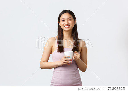 Lifestyle, people emotions and glamour concept. Gorgeous young korean girl in stylish dress, drinking coffee and smiling as talking to coworker, holding mug, standing white background Lifestyle, people emotions and glamour concept. Gorgeous young korean girl in stylish dress, drinking coffee and smiling as talking to coworker, holding mug, standing white background 71807825