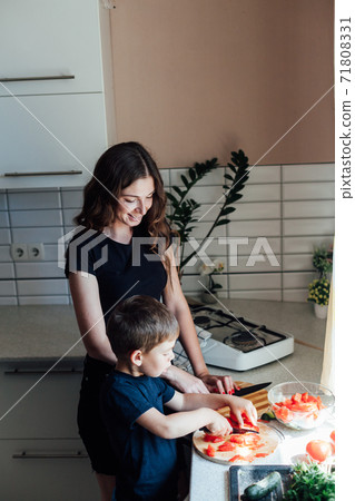 Mom and young son cut vegetables for salad in the kitchen Mom and young son cut vegetables for salad in the kitchen 71808331