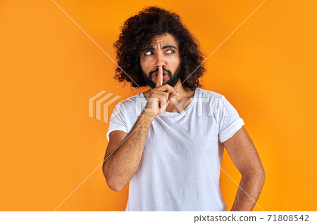 young arab man raising his finger on the front of his mouth askingto be quite 71808542