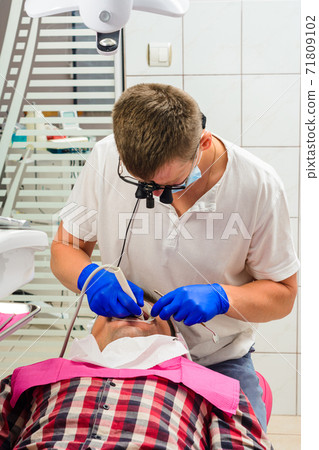 Dentist in the clinic,tartar removal procedure,the dentist in binoculars removes tartar in the patient's mouth. 71809102