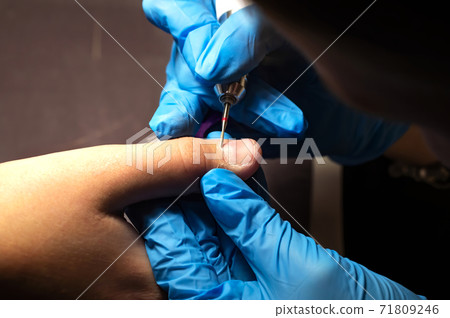 manicurist in blue gloves does a hardware manicure, mechanical processing of nails with a cutter, cuticle removal with an apparatus, professional manicure in a beauty salon. Hand care concept 71809246