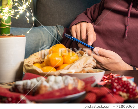 Closeup view of man with mobile phone sitting near Christmas decorated table  71809366