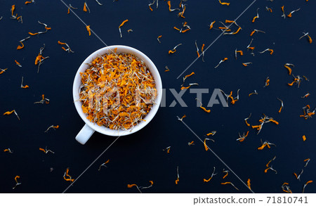 White cup with dry marigold flower petals on dark background. Herbal tea concept. White cup with dry marigold flower petals on dark background. Herbal tea concept. 71810741