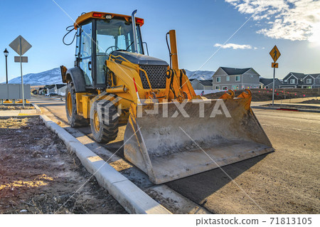 Yellow loader with homes and mountain against blue sky in the background Yellow loader with homes and mountain against blue sky in the background 71813105