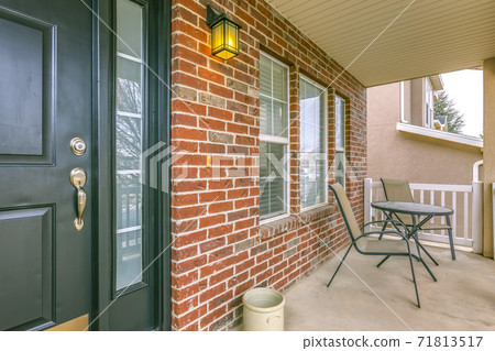 Front porch of a home with table and chairs in front of brick wall and window 71813517