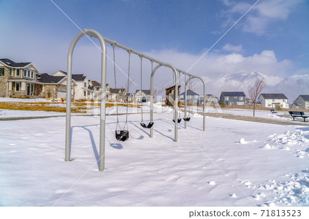 Baby swings at a playground blanketed with clean snow on a sunny winter day Baby swings at a playground blanketed with clean snow on a sunny winter day 71813523