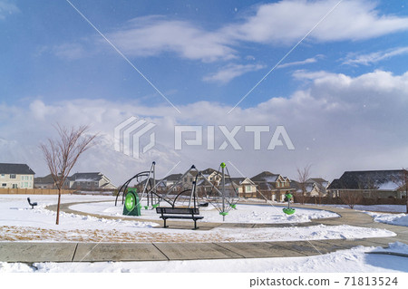 Playground and bench on a snowy playground against homes in winter Playground and bench on a snowy playground against homes in winter 71813524
