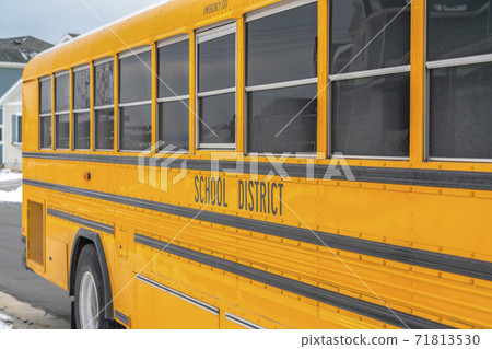 Close up of a yellow school bus on a snowy road against homes and cloudy sky Close up of a yellow school bus on a snowy road against homes and cloudy sky 71813530