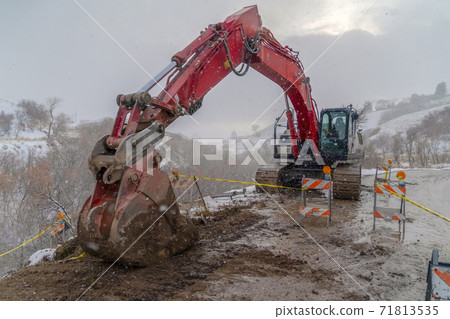 Excavator on a muddy road with barricades and yellow tape viewed in winter Excavator on a muddy road with barricades and yellow tape viewed in winter 71813535