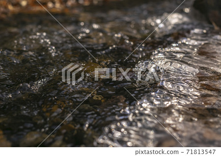 Close up of a stream with translucent frozen water over dark rocks Close up of a stream with translucent frozen water over dark rocks 71813547