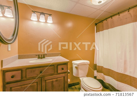 Toilet and vanity with wooden cabinet and round mirror inside a bathroom 71813567