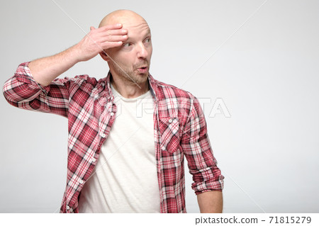 Funny, shocked bald man, with a bizarre expression on face, holds hand near head and looks surprised Funny, shocked bald man, with a bizarre expression on face, holds hand near head and looks surprised 71815279
