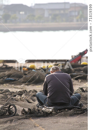 A man who cares for fishing nets spread on the quay 71819399
