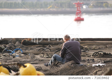 A man who cares for fishing nets spread on the quay 71819402